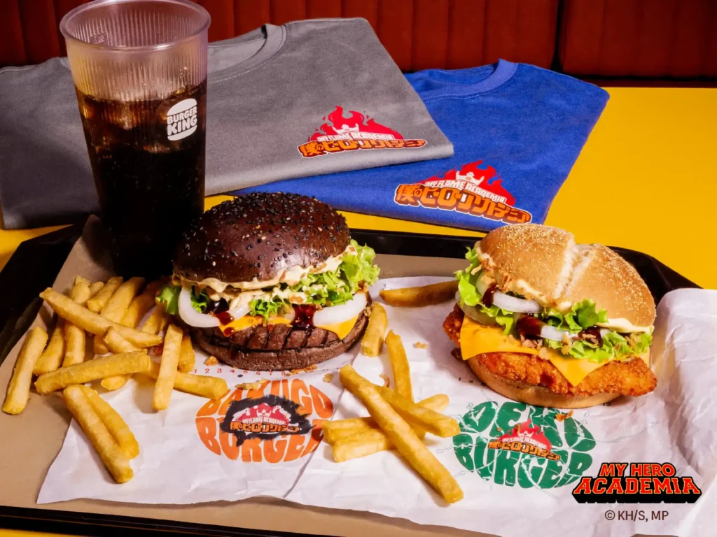 Due burger a tema My Hero Academia di Burger King: uno chiamato "Bakugo Burger" con pane nero e l'altro "Deku Burger" con pane classico, serviti con patatine fritte e una bevanda.