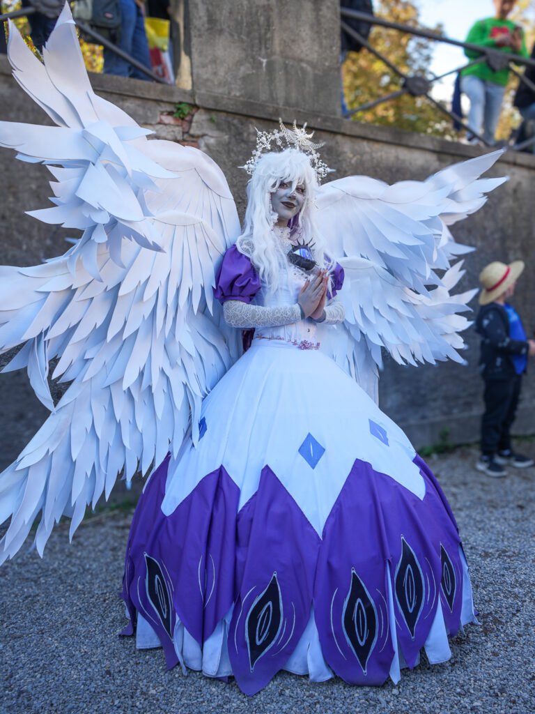Cosplayer in costume angelico con ali bianche e abito viola alla Lucca Comics & Games 2024.